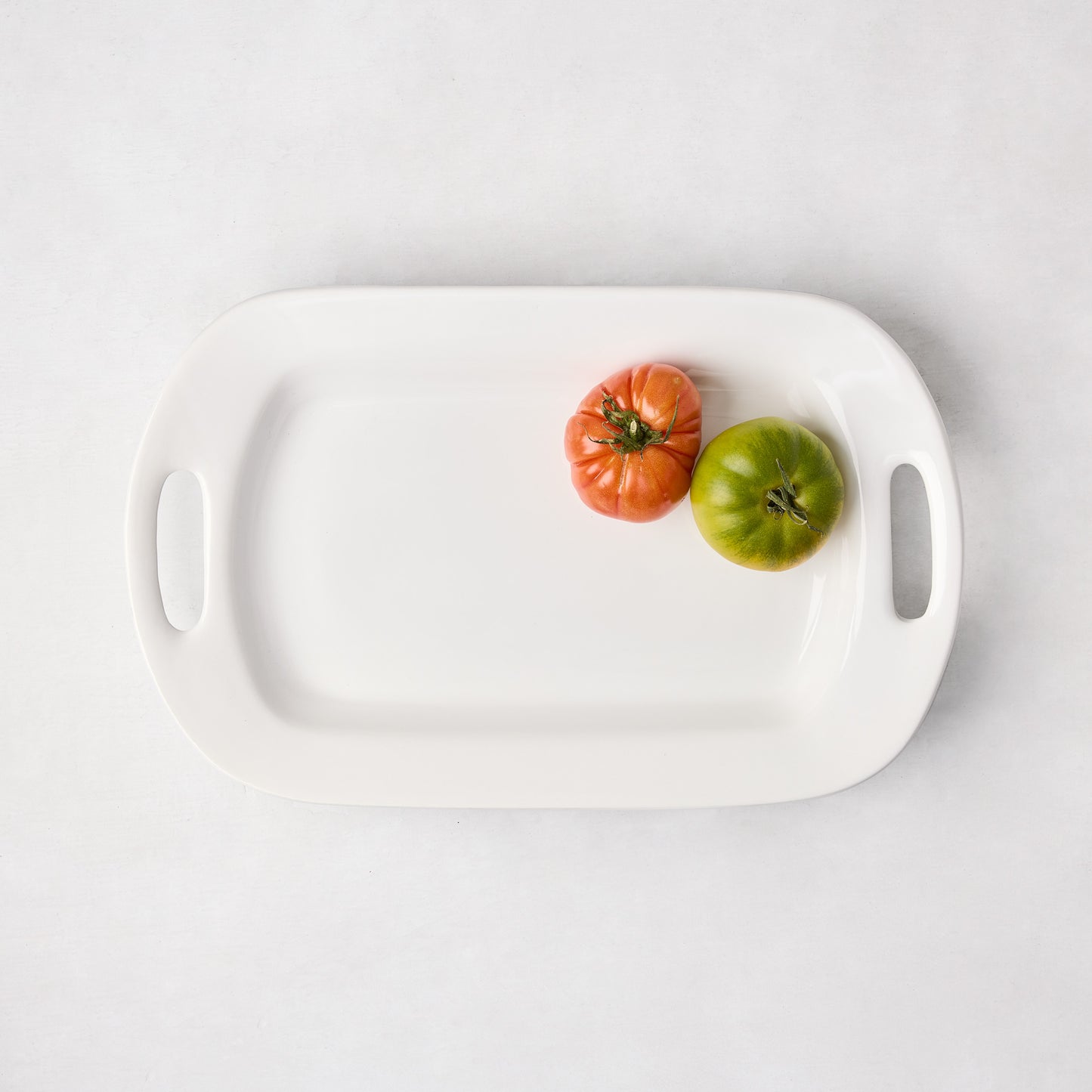 White ceramic handled serving platter with two heirloom tomatoes.