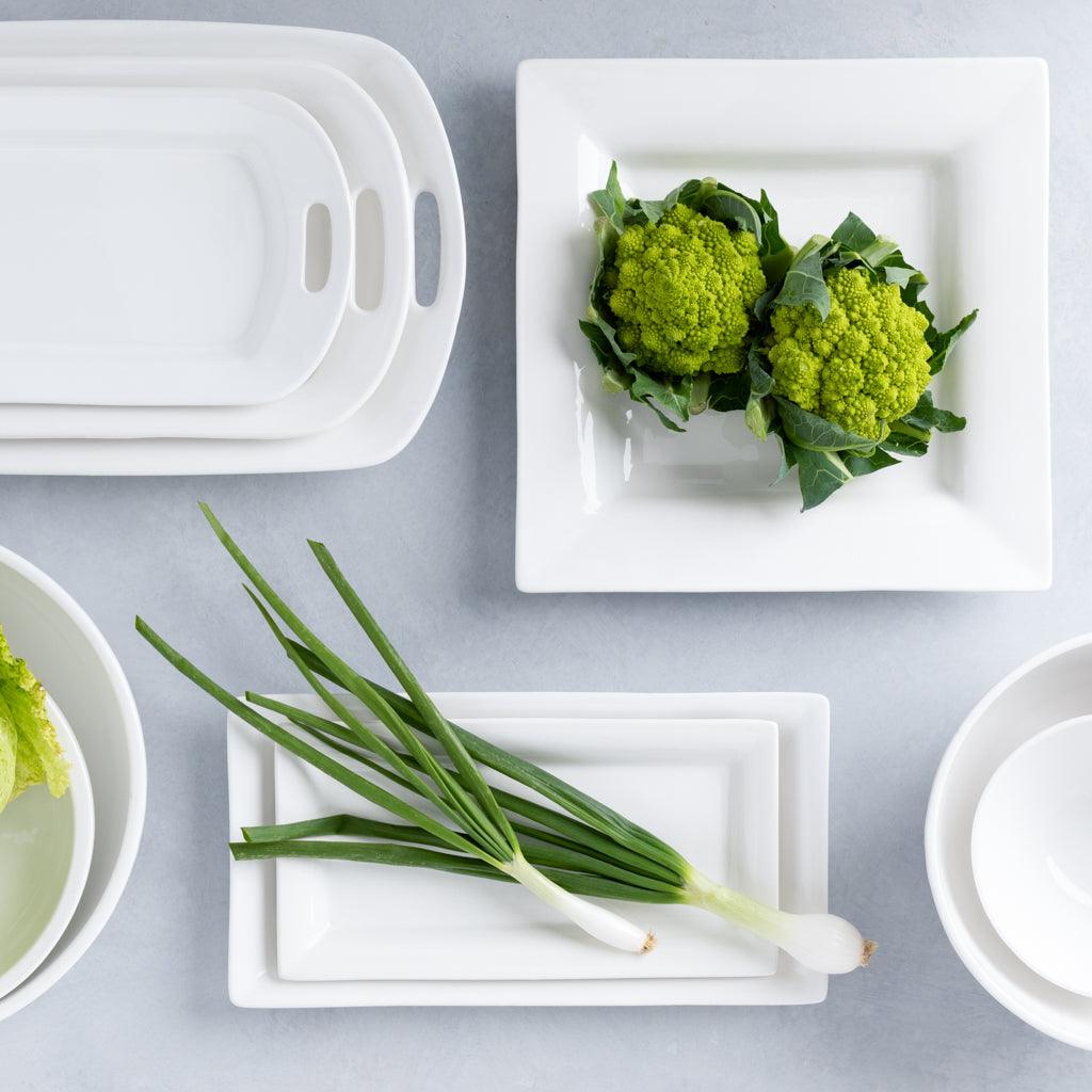 White ceramic handled serving platter, rectangular dishes, and square plates with green vegetables.