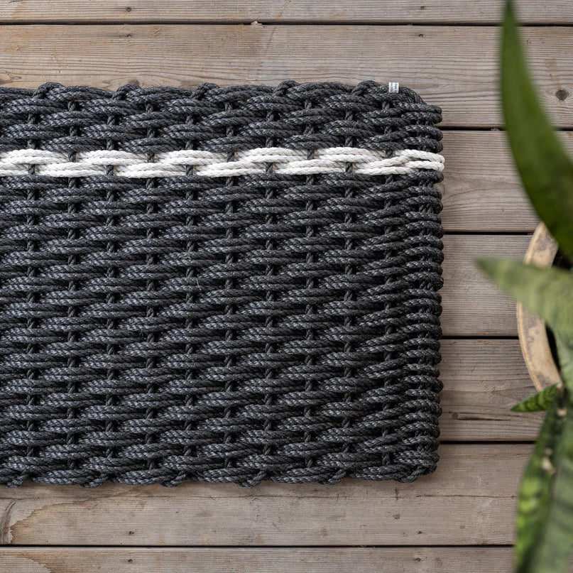 Handwoven charcoal rope doormat with a single white pearl stripe, on a wooden deck.