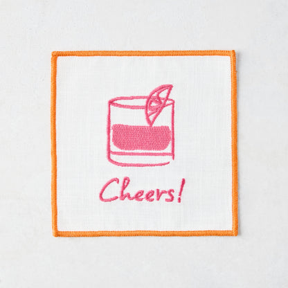 White cotton coaster with orange trim, pink embroidered cocktail and "Cheers!" text.