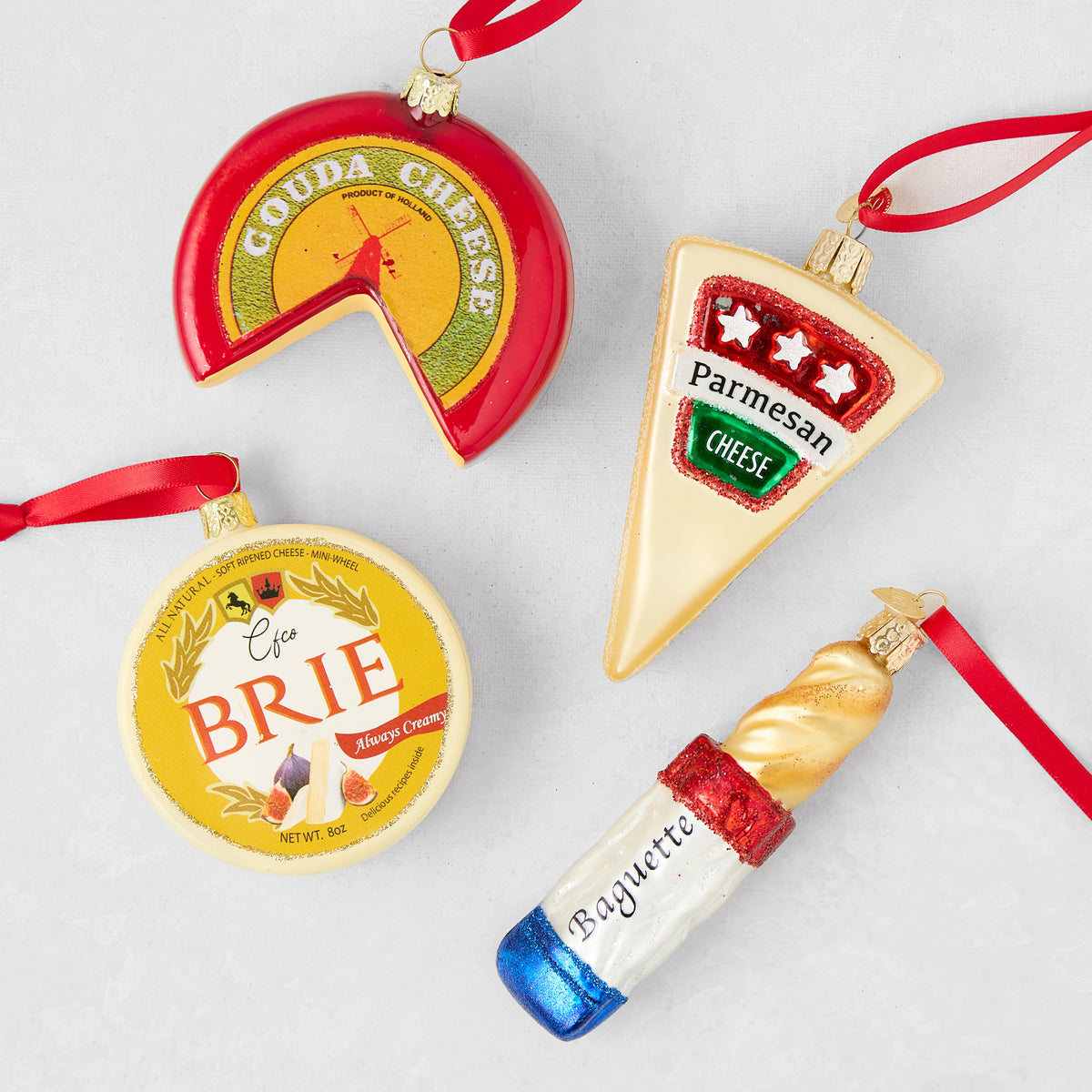 Glass cheese and baguette Christmas ornaments including Gouda, Brie, Parmesan, and bread with red hanging ribbons.