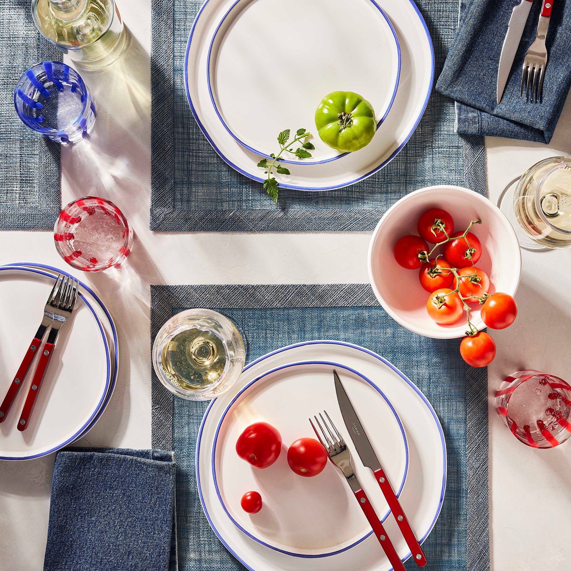 Cherry red bistro flatware set with stainless steel and acrylic handles arranged on a table with plates and tomatoes.