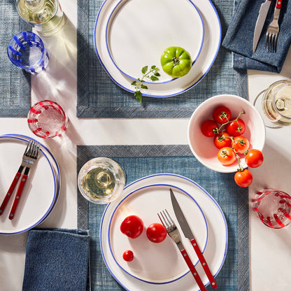 Cherry red bistro flatware set with stainless steel and acrylic handles arranged on a table with plates and tomatoes.