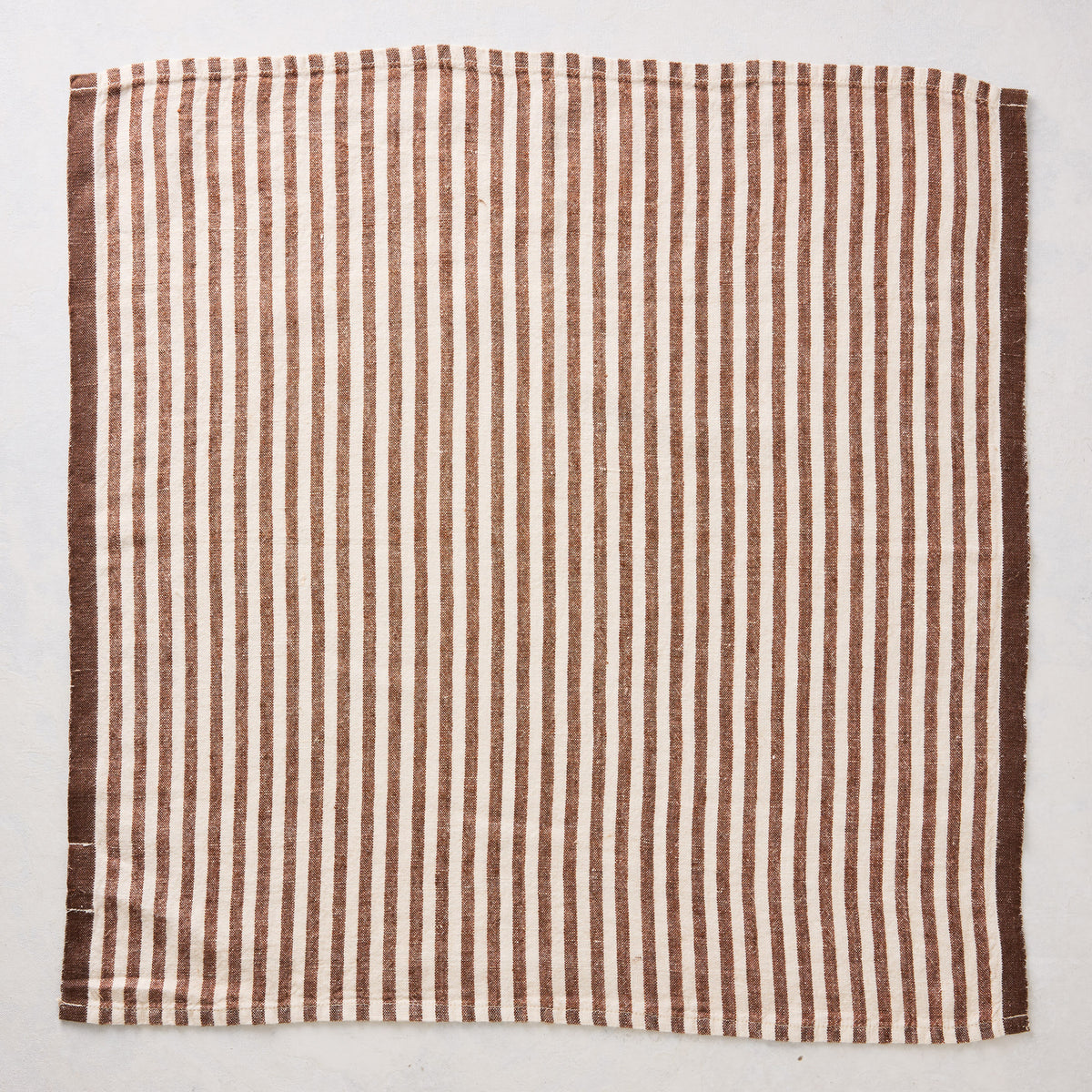 21-inch square napkin with brown and white ticking stripes and a solid brown border, made from textured linen fabric.