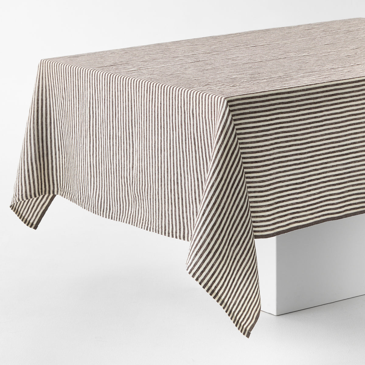 Chocolate brown and white ticking stripe linen tablecloth with a brown border on a white table.