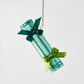 Light blue Christmas cracker ornament with green glitter stripes and dark green ribbon bows hanging on a gold string.