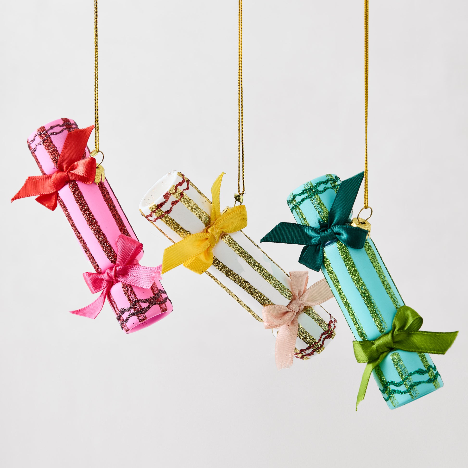 Three hanging Christmas cracker ornaments in pink, white, and teal, featuring glittered stripes and satin bows.