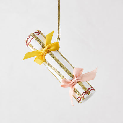 White Christmas cracker ornament with gold glitter stripes, red accents, and yellow and pink ribbon bows.