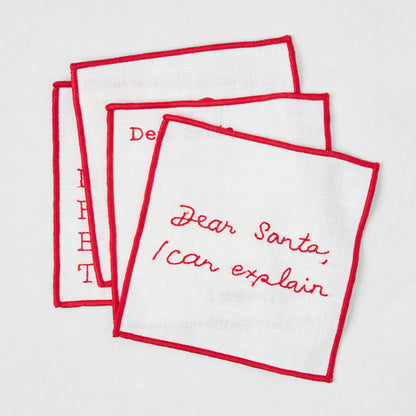 Set of four 5.5-inch square white cotton coasters with red embroidered Christmas phrases and red stitched borders.