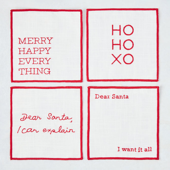 Set of four 5.5-inch square white cotton coasters with red embroidered Christmas phrases and red stitched borders.
