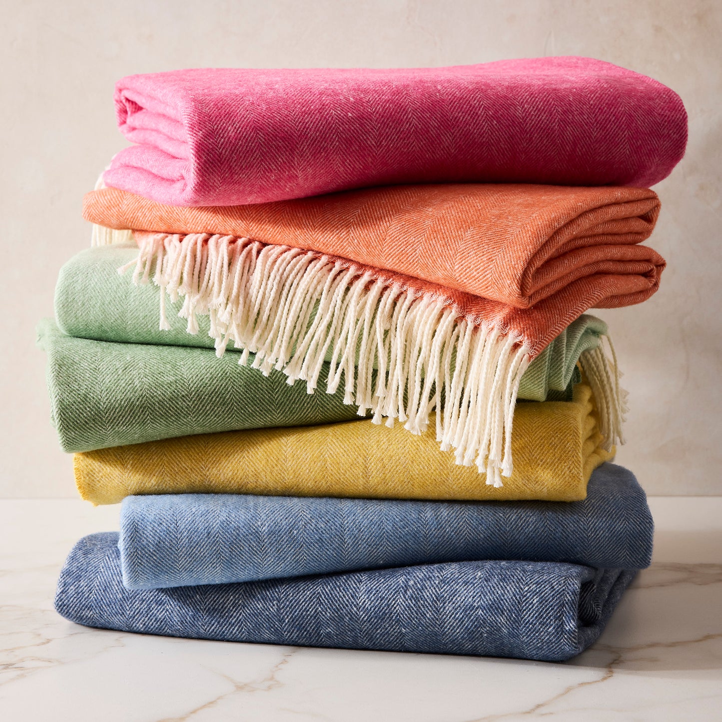 Stacked Italian Herringbone throw blankets in pink, orange, green, yellow, and blue with fringe.