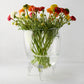 Large Cis clear glass bowl with scissor-cut rim, on three legs, holding colorful ranunculus flowers.