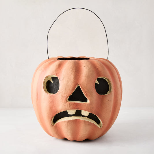 Handcrafted, distressed orange papier-mâché Jack O' Lantern candy bucket with a sad face and black wire handle.