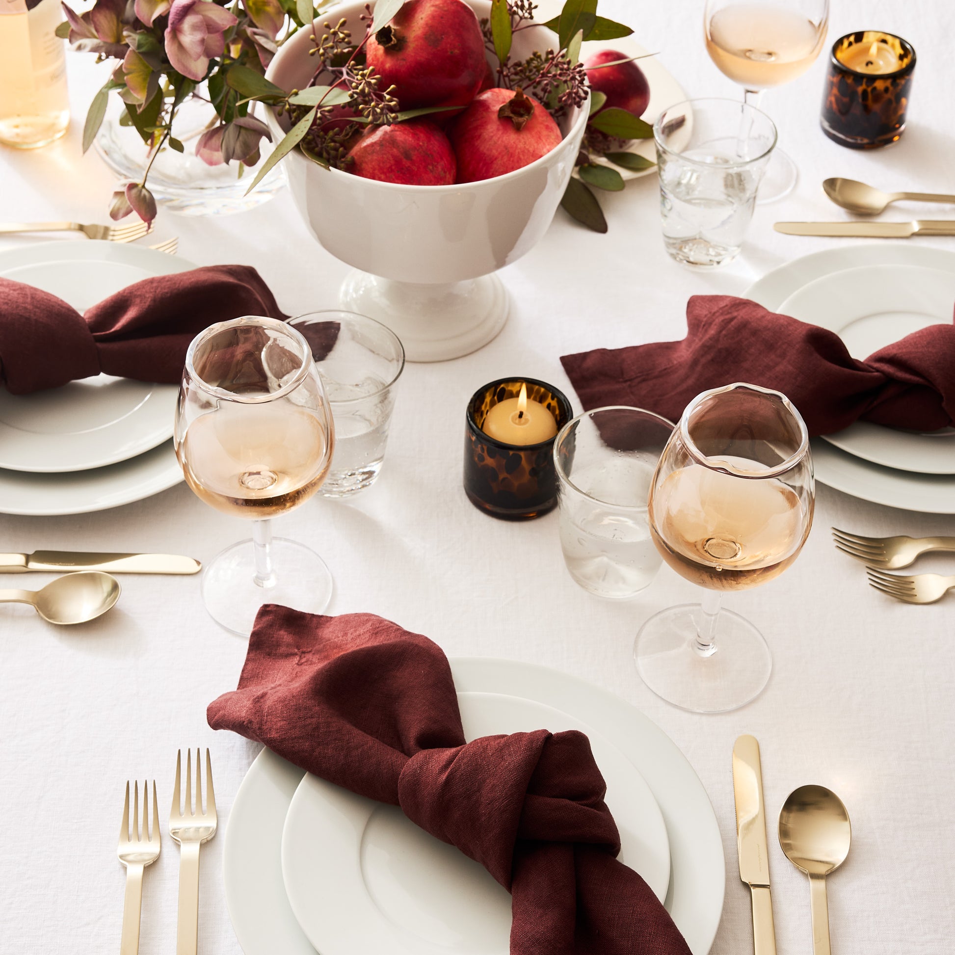 White HG Classic Porcelain Salad Plate on a set table with burgundy napkins, gold flatware, and pomegranates.