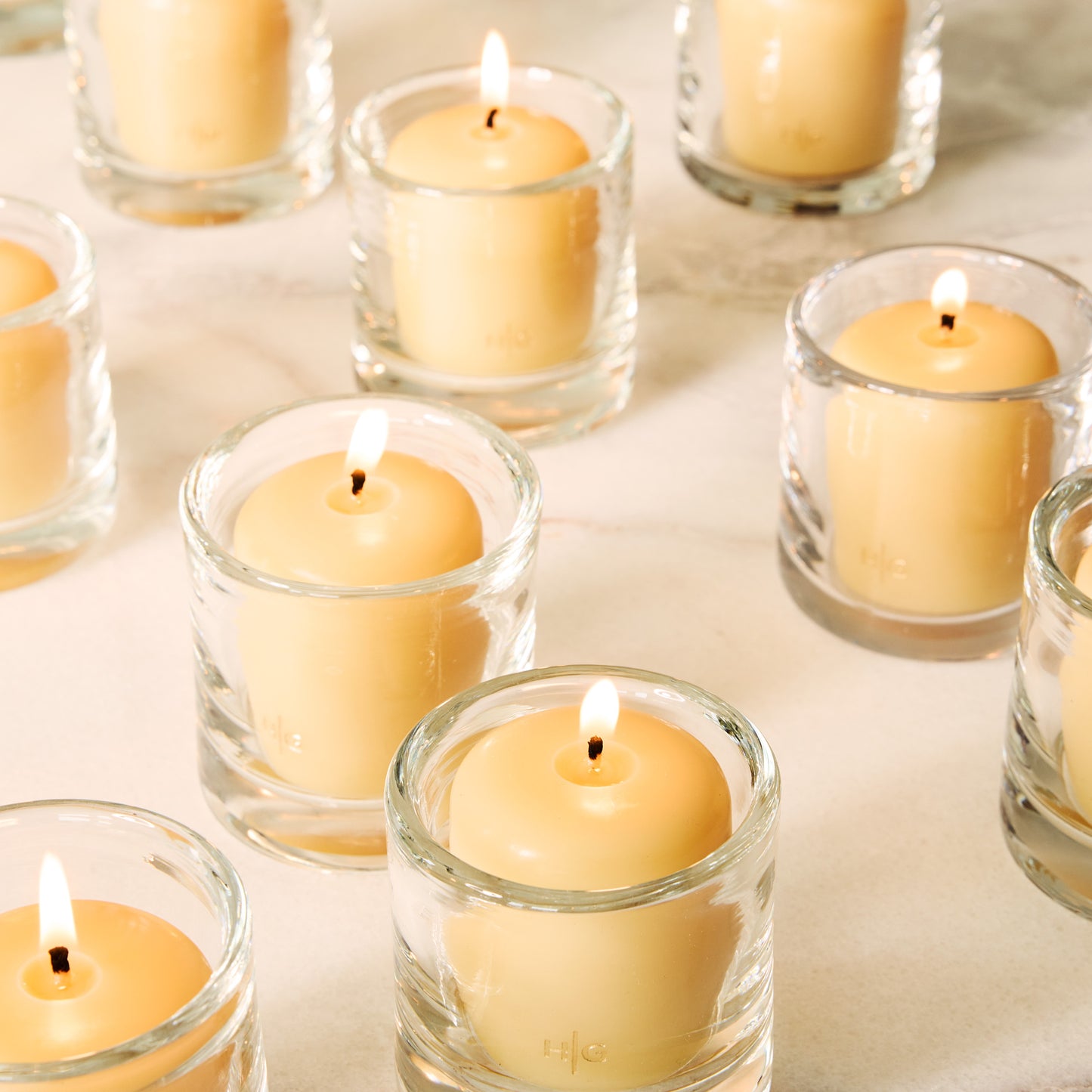 Clear glass votive candle holders with lit amber votive candles on a light surface.
