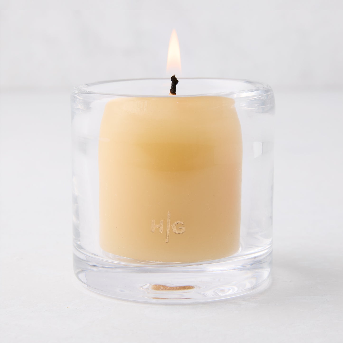 Clear glass votive candle holder with a lit amber votive candle, 2.75"Dia x 2.75"H.