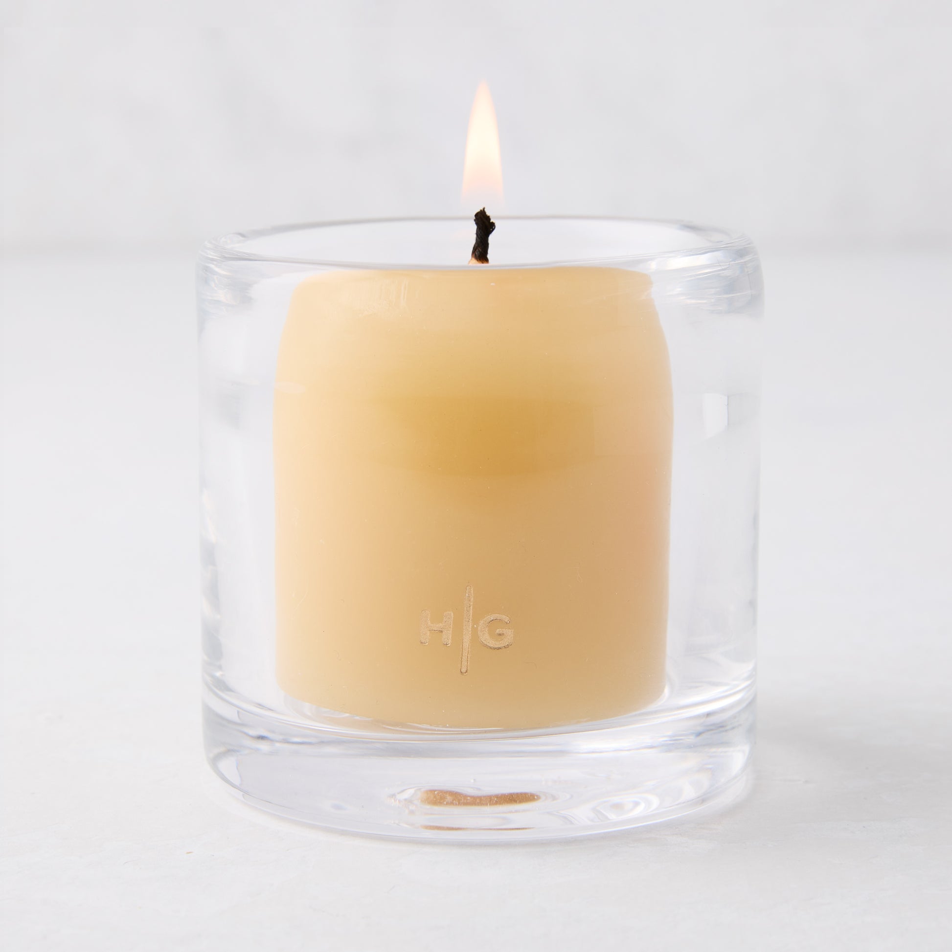 Clear glass votive candle holder with a lit amber votive candle, 2.75"Dia x 2.75"H.