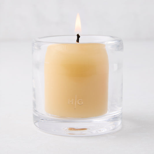 Clear glass votive candle holder with a lit amber votive candle, 2.75"Dia x 2.75"H.