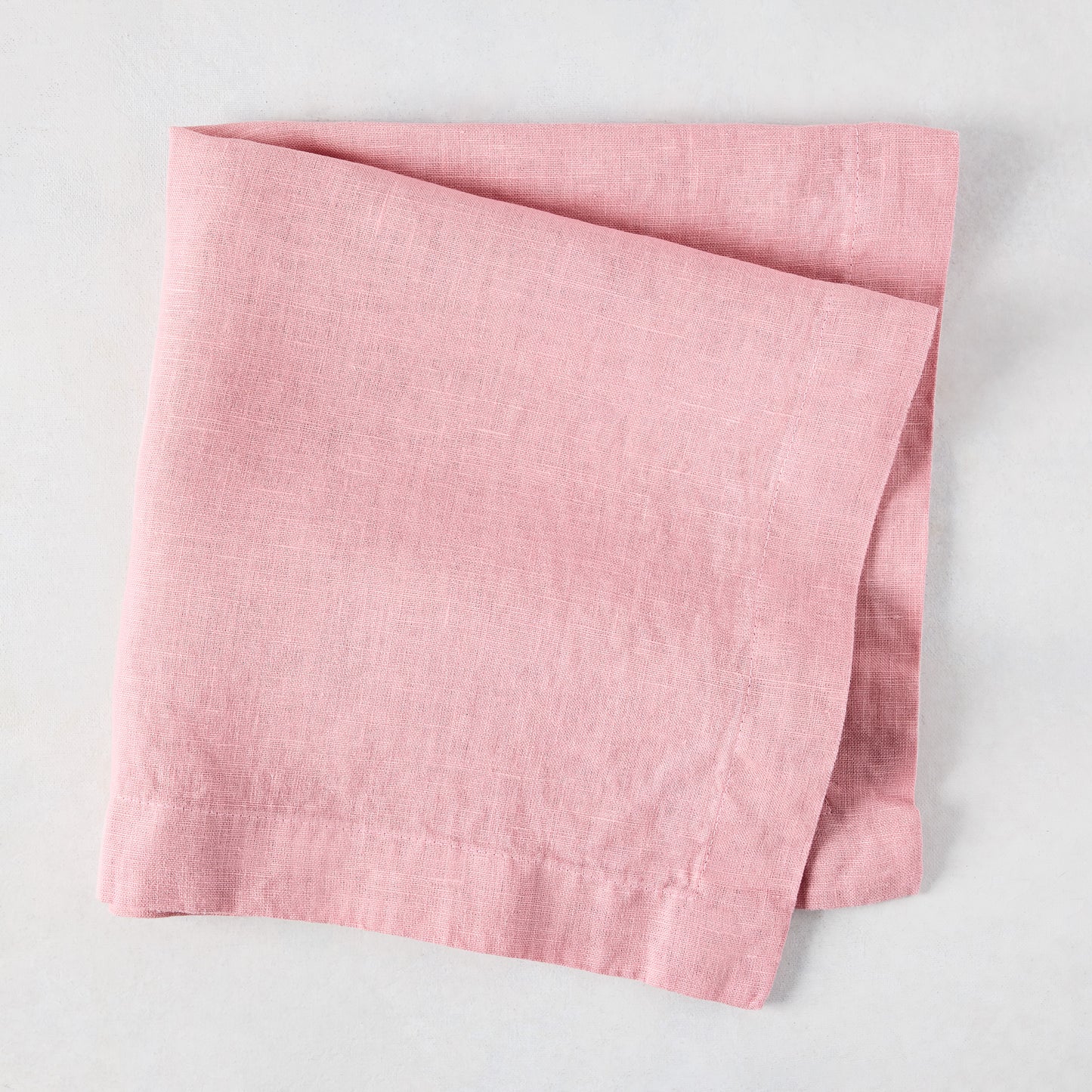Clover Pink HG Signature hand-dyed linen napkin, 22-inch square, folded on a light surface.