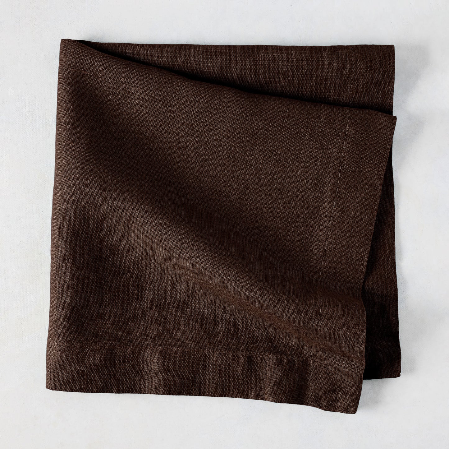 Cocoa HG hand-dyed 22" square brown linen napkin, folded on a light surface.