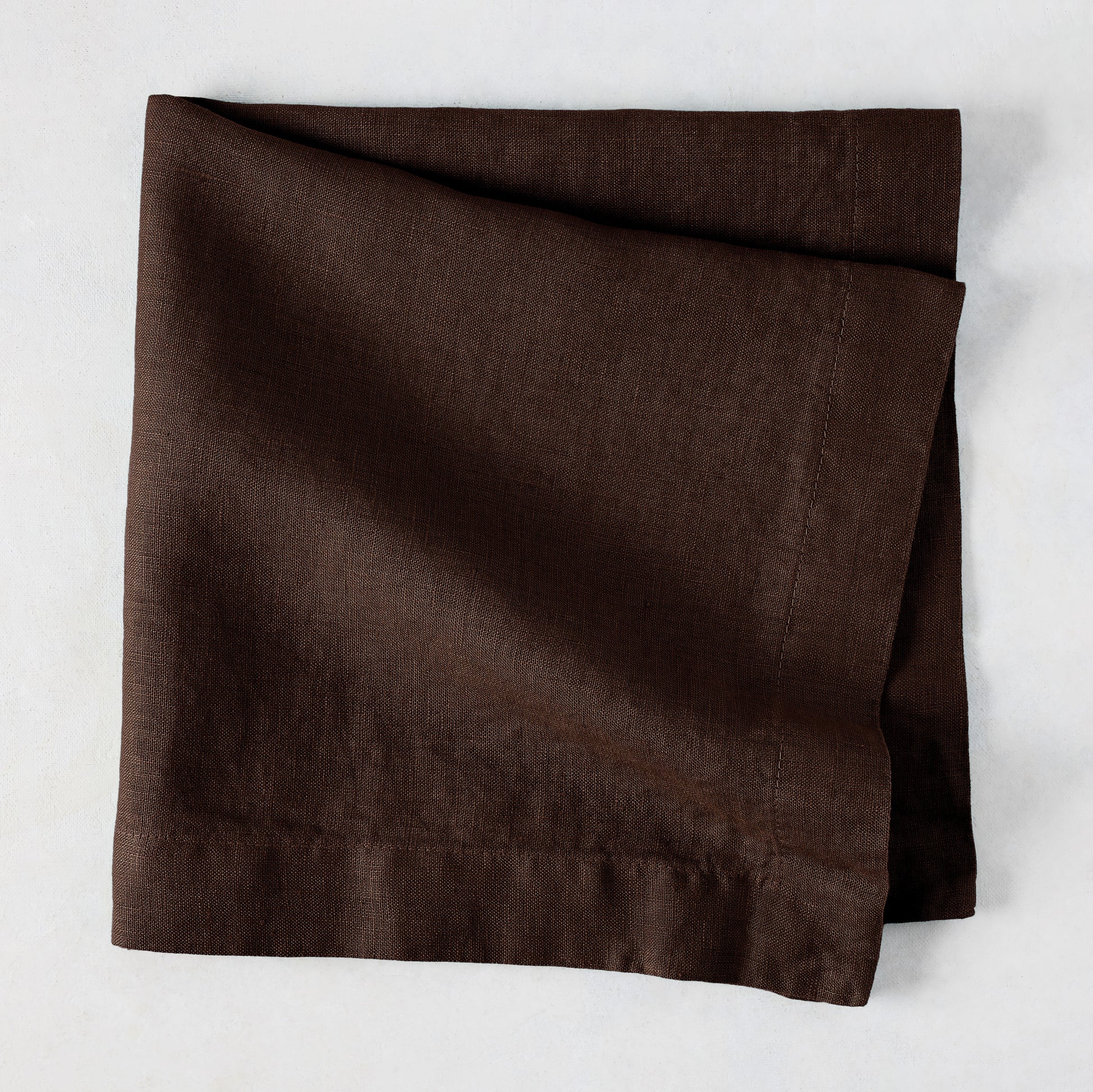 Cocoa HG hand-dyed 22" square brown linen napkin, folded on a light surface.