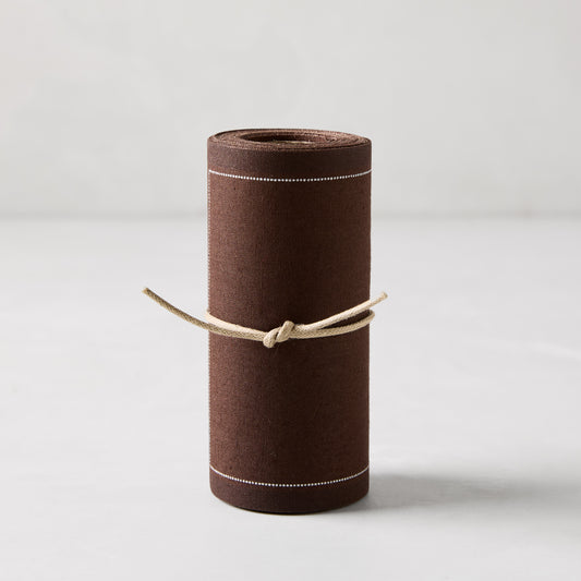 Roll of 50 cocoa brown cotton tear-off cocktail napkins with white dashed lines, tied with twine.