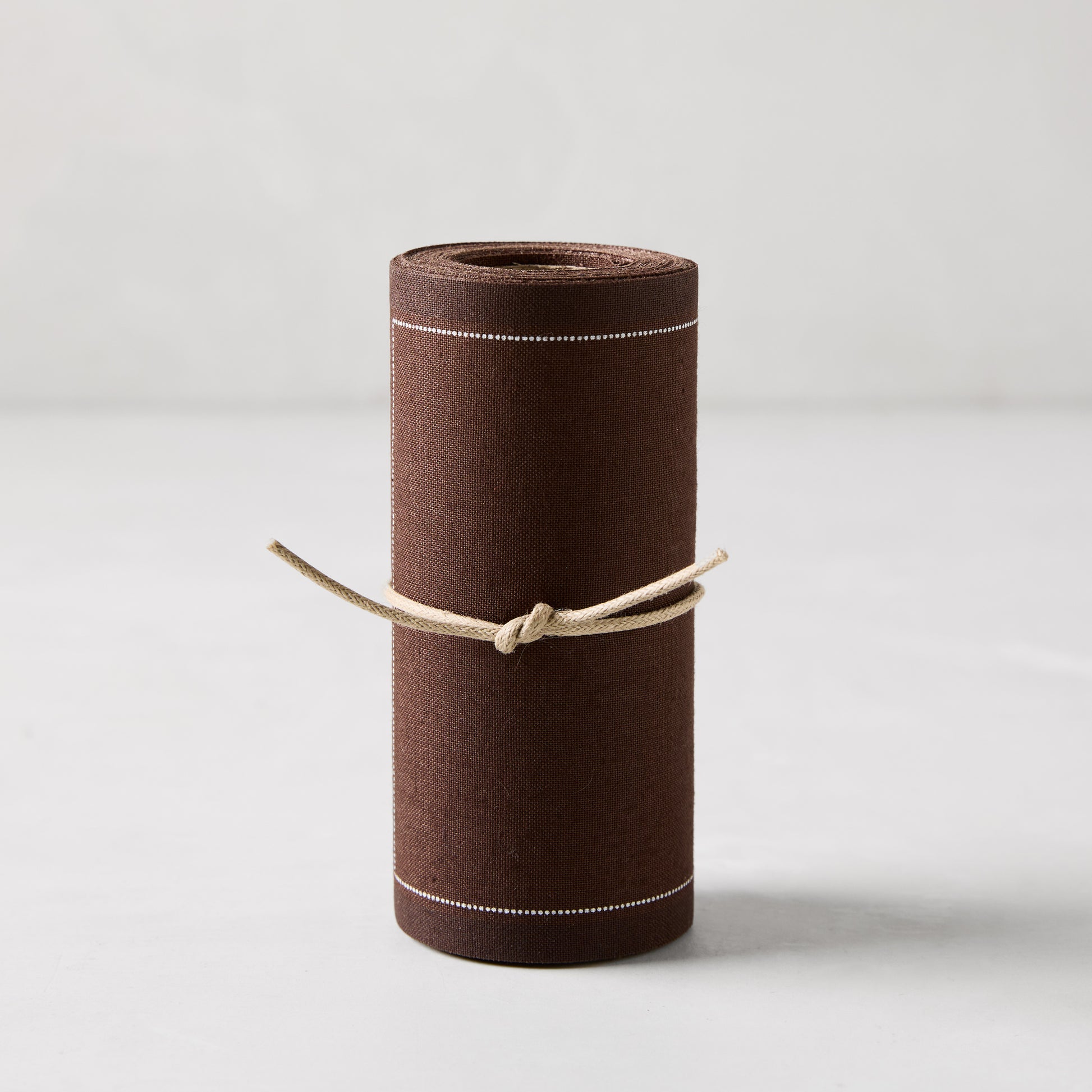Roll of 50 cocoa brown cotton tear-off cocktail napkins with white dashed lines, tied with twine.
