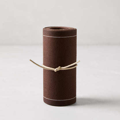 Roll of 50 cocoa brown cotton tear-off cocktail napkins with white dashed lines, tied with twine.