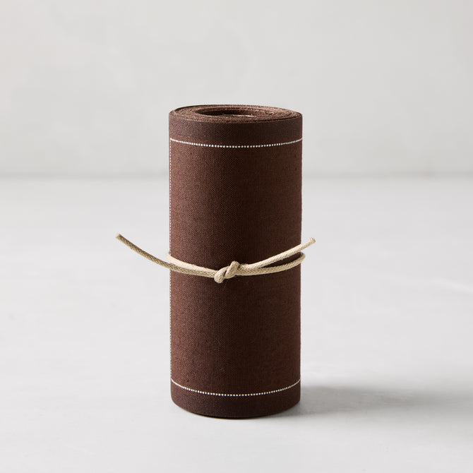 Roll of 50 cocoa brown cotton tear-off cocktail napkins with white dashed lines, tied with twine.