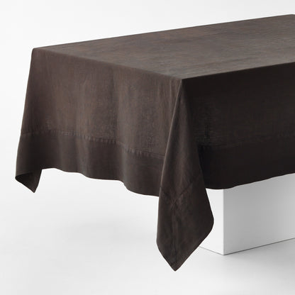 Cocoa brown hand-dyed linen tablecloth with a wide border and mitered corner detailing on a white table.
