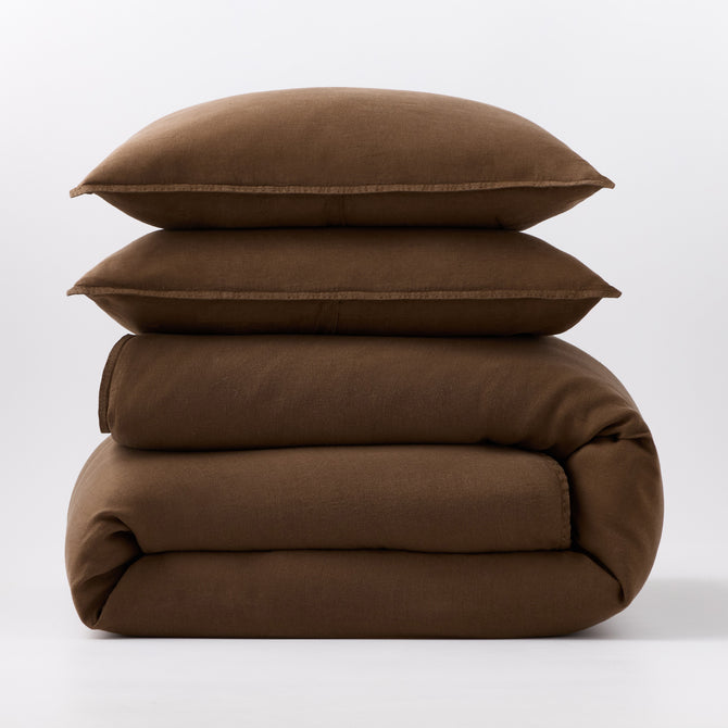 Stacked coffee brown European washed linen duvet and two matching pillow shams on a white background.