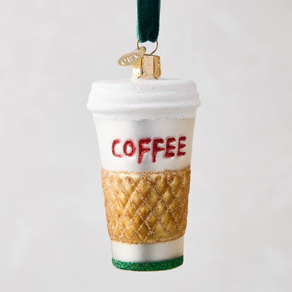 White glass coffee cup ornament with "COFFEE" in red glitter, gold quilted sleeve, and green glitter base.