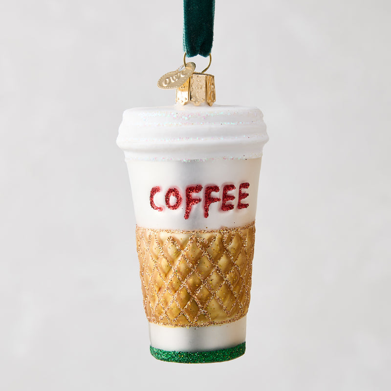 White glass coffee cup ornament with "COFFEE" in red glitter, gold quilted sleeve, and green glitter base.