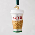 White glass coffee cup ornament with "COFFEE" in red glitter, gold quilted sleeve, and green glitter base.