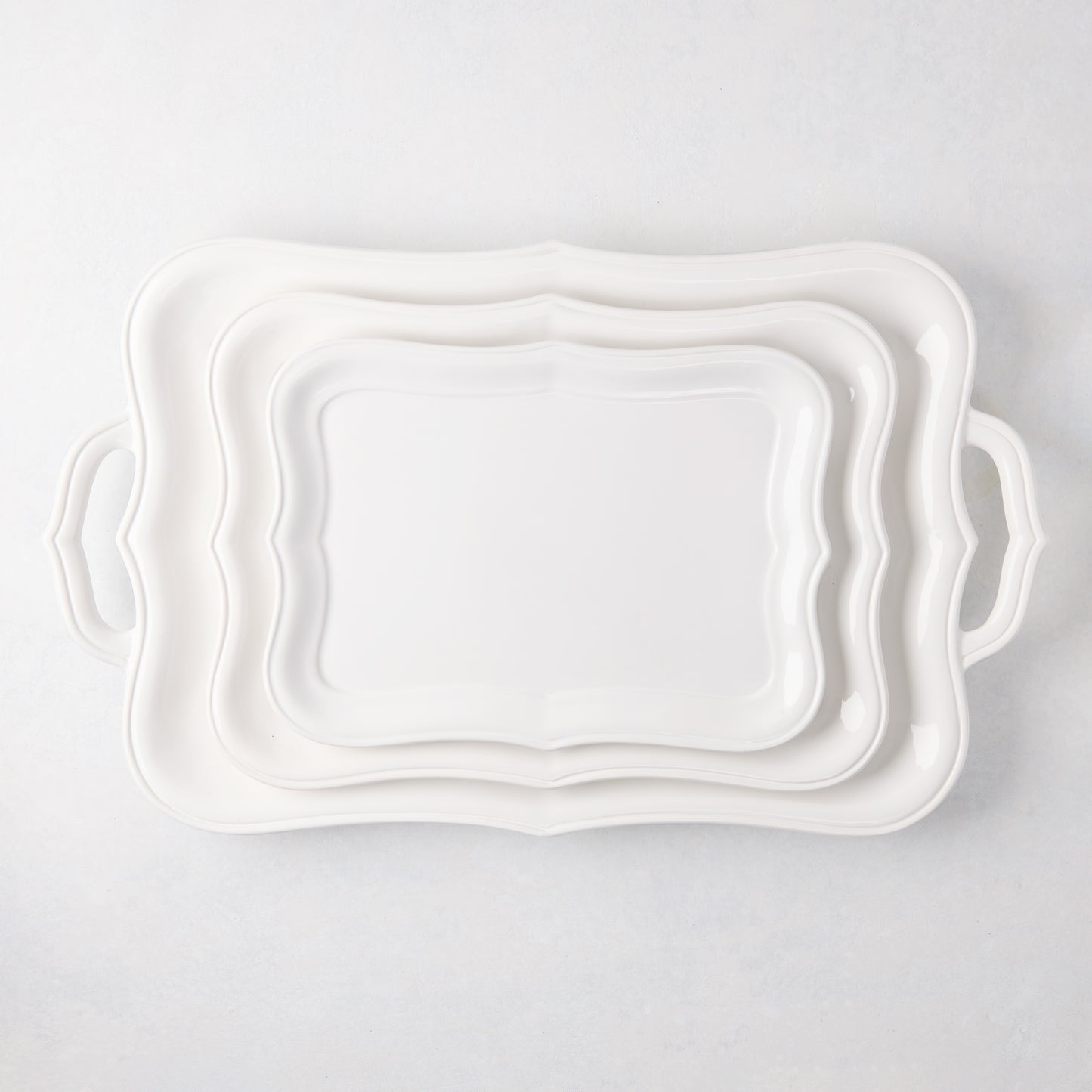 Three stacked white ceramic serving platters with scalloped edges and handles.