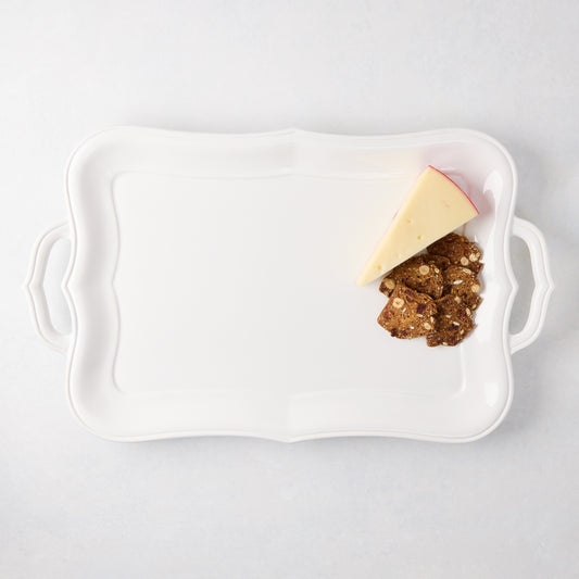 White ceramic Colette serving platter with scalloped edges and handles, holding cheese and crackers.