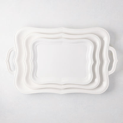Three stacked white Colette ceramic serving platters with scalloped edges.
