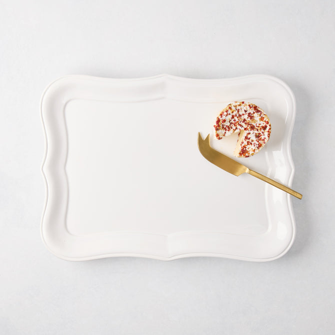 Colette Medium white ceramic serving platter with scalloped edges, a cheese wheel, and gold knife.