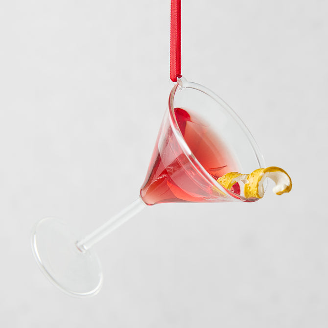 Handmade glass Cosmopolitan Christmas tree ornament with red liquid, lemon twist, and red ribbon.