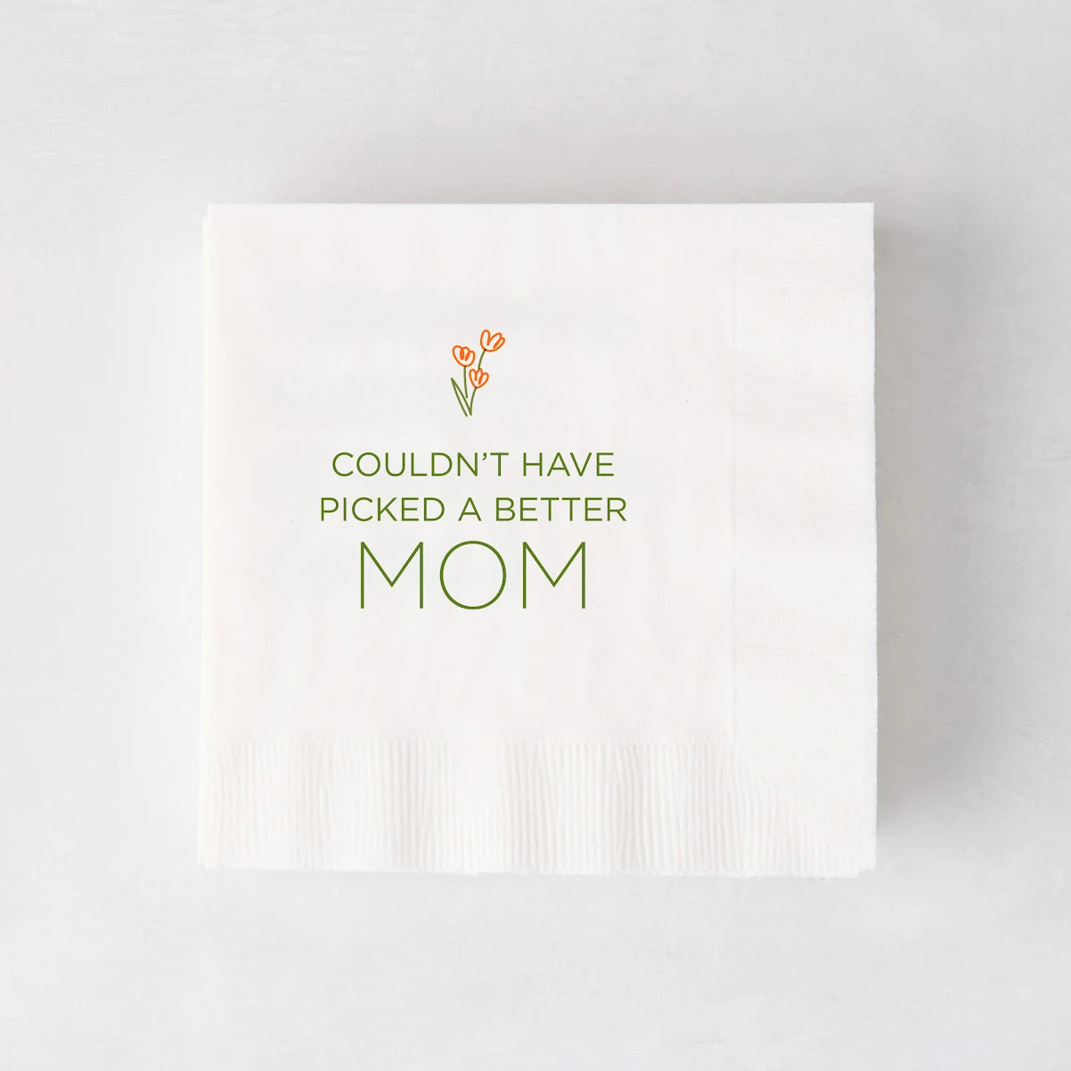 White paper cocktail napkin with "Couldn't Have Picked a Better Mom" in green, topped with orange tulips.
