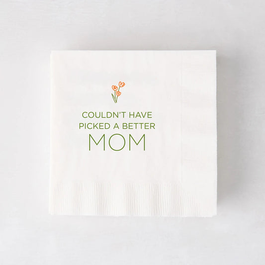 White paper cocktail napkin with "Couldn't Have Picked a Better Mom" in green, topped with orange tulips.