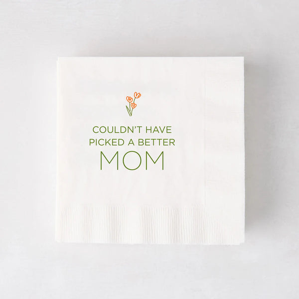 White paper cocktail napkin with "Couldn't Have Picked a Better Mom" in green, topped with orange tulips.