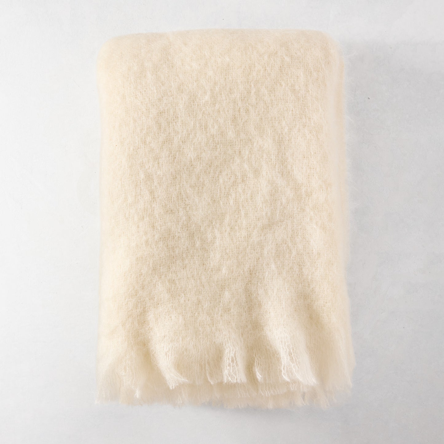 Folded cream mohair throw blanket with fringe, 72"L x 51"W.