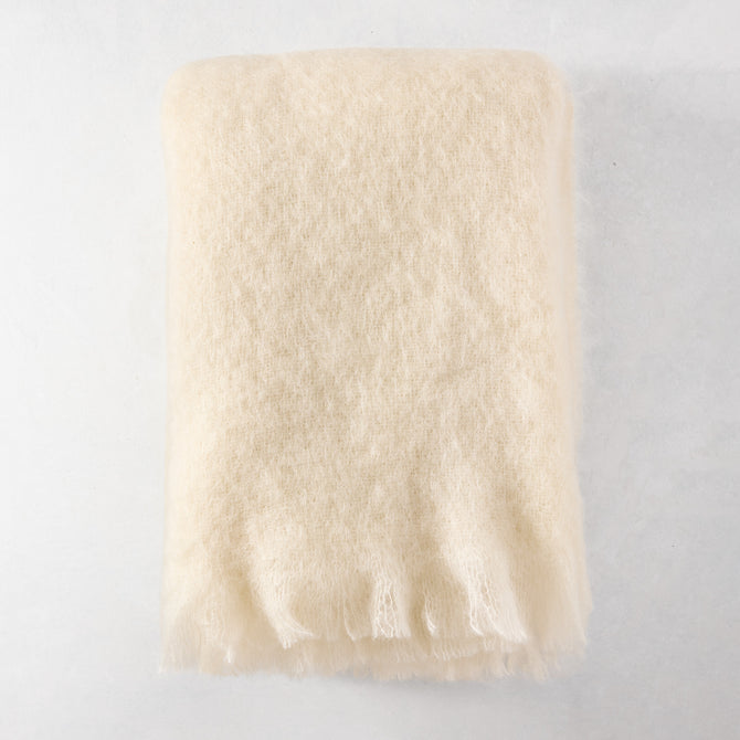 Folded cream mohair throw blanket with fringe, 72"L x 51"W.