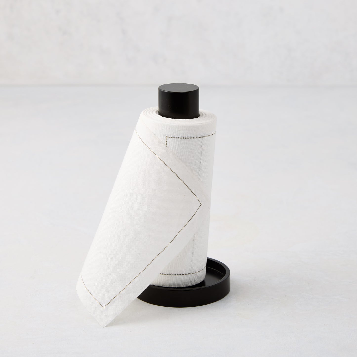 Cream tear-off napkins with gray stitching in a black metal napkin holder.