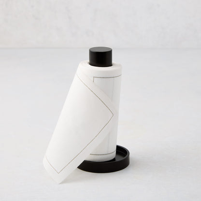 Cream tear-off napkins with gray stitching in a black metal napkin holder.