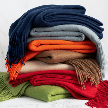 Stack of folded cashmere throw blankets in navy, grey, orange, tan, cream, red, and lime green with fringe.