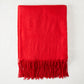 Crimson cashmere throw blanket with fringe, folded on a white surface.