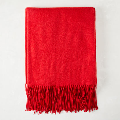 Crimson cashmere throw blanket with fringe, folded on a white surface.