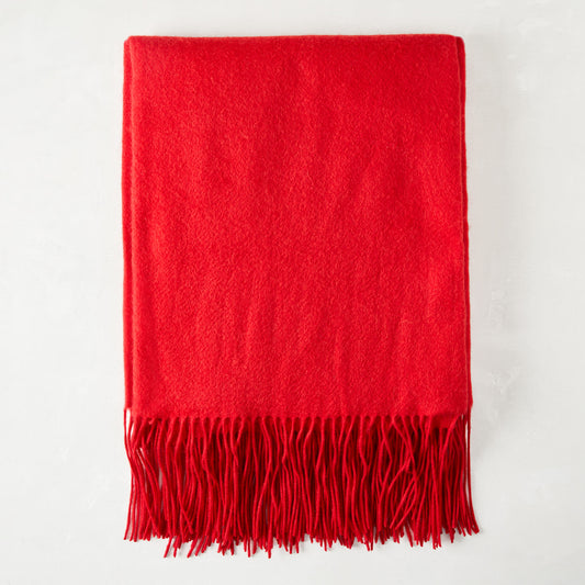 Crimson cashmere throw blanket with fringe, folded on a white surface.